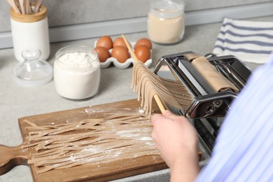 Photo of Woman making soba with pasta machine at table in kitchen, closeup