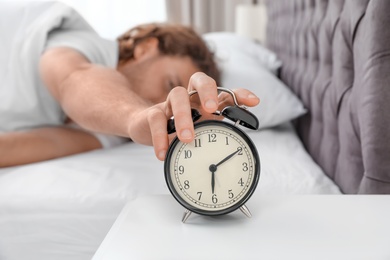 Photo of Sleepy man turning off alarm clock in morning. Bedtime