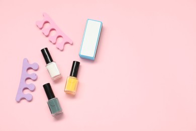 Photo of Nail polishes, toe separators and buffer on pink background, flat lay. Space for text