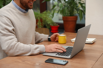 Male blogger working with laptop at table in cafe, closeup