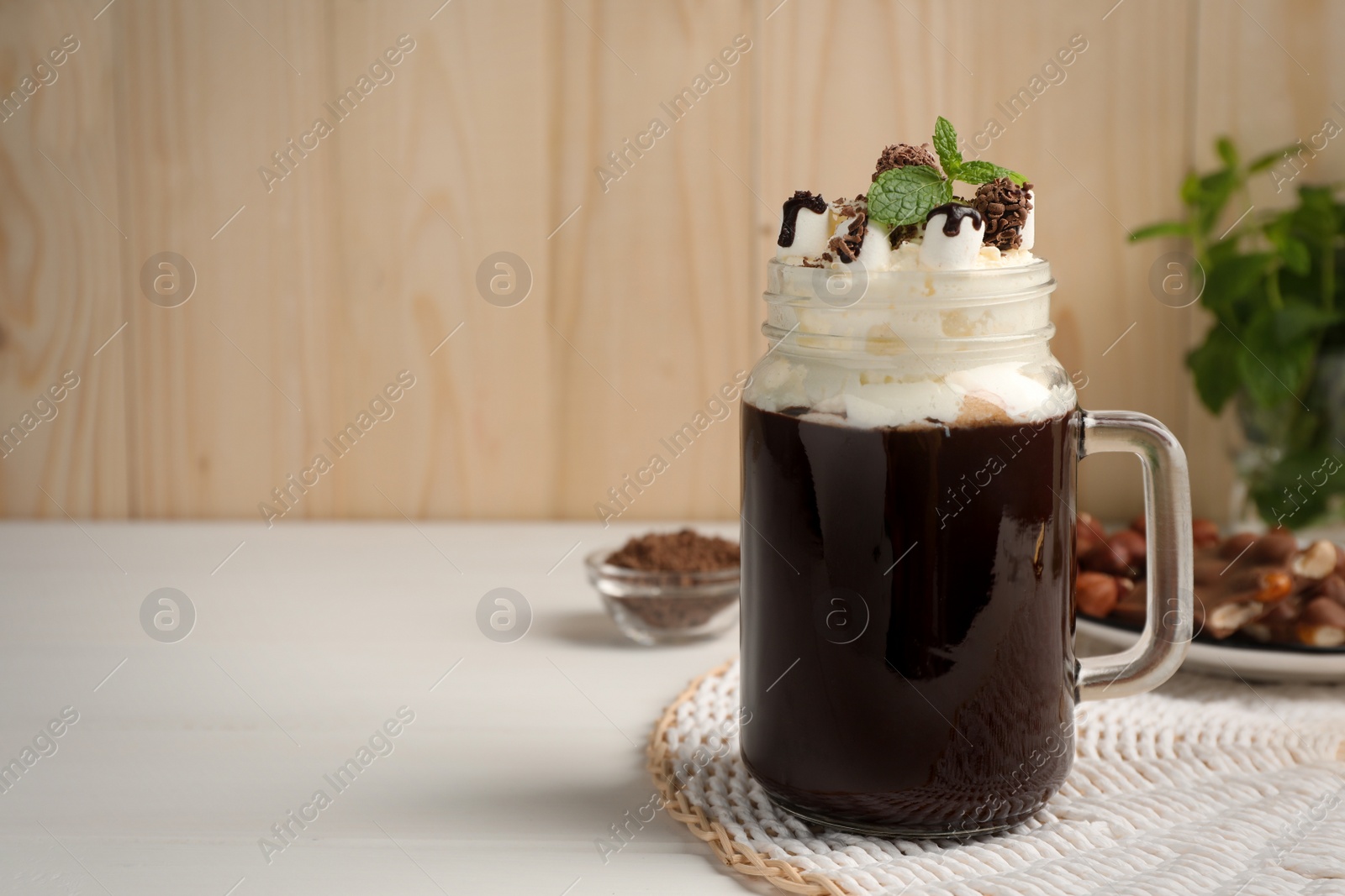 Photo of Mason jar of delicious hot chocolate with whipped cream and mint on white wooden table. Space for text