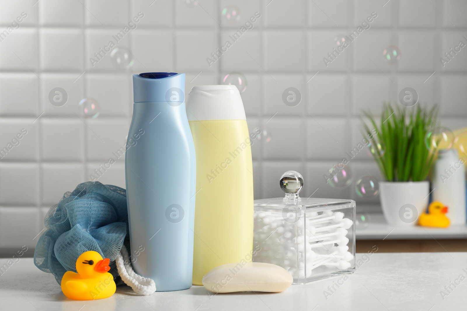 Photo of Baby cosmetic products, bath duck, sponge and cotton swabs on white table against soap bubbles. Space for text