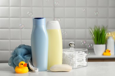 Baby cosmetic products, bath duck, sponge and cotton swabs on white table against soap bubbles. Space for text