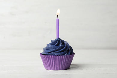 Delicious birthday cupcake with cream and burning candle on white wooden table