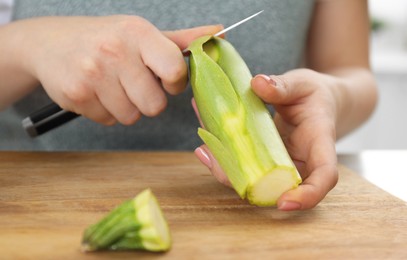 Photo of Woman peeling fresh zucchini with knife at table, closeup