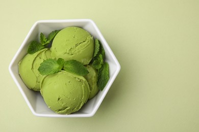 Tasty matcha ice cream with mint in bowl on pale green background, top view. Space for text
