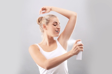 Photo of Young woman using deodorant on grey background