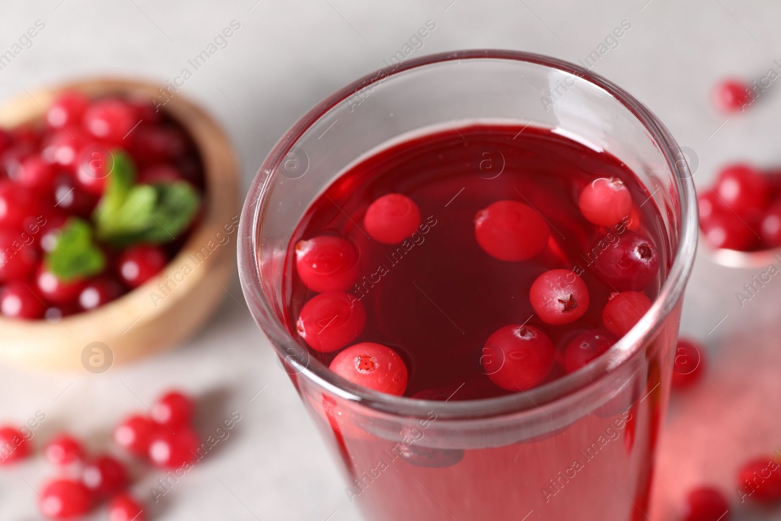 Photo of Tasty cranberry juice in glass and fresh berries on light grey table, closeup