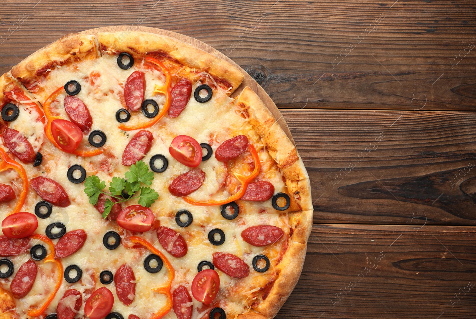 Photo of Tasty pizza with dry smoked sausages, tomato, olives, pepper and parsley on wooden table, top view. Space for text