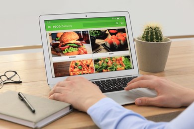 Photo of Man using laptop for ordering food online at table indoors, closeup. Concept of delivery service