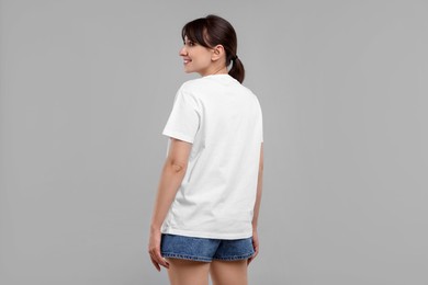 Photo of Smiling woman in white t-shirt on grey background, back view