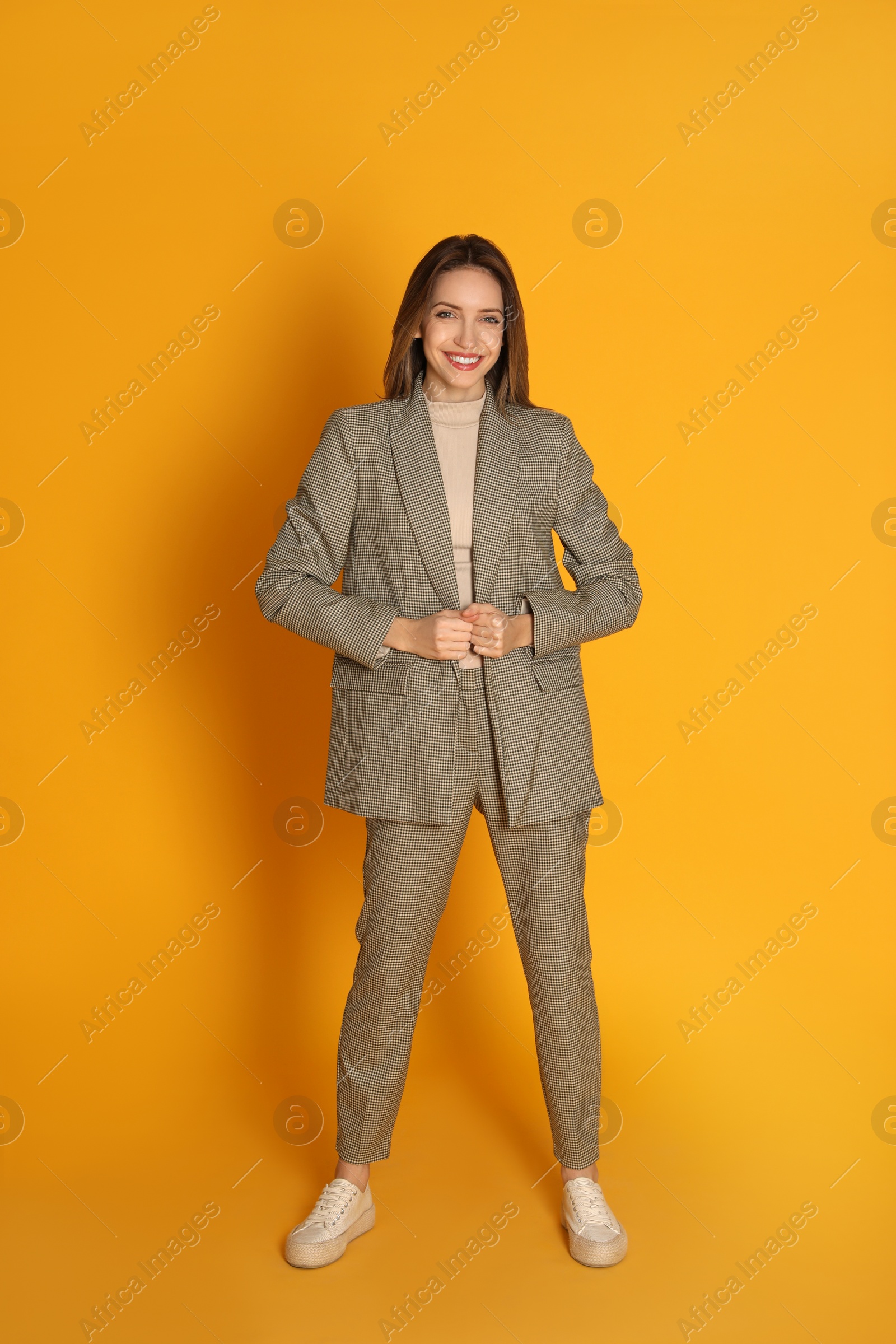 Photo of Full length portrait of beautiful young woman in fashionable suit on yellow background. Business attire