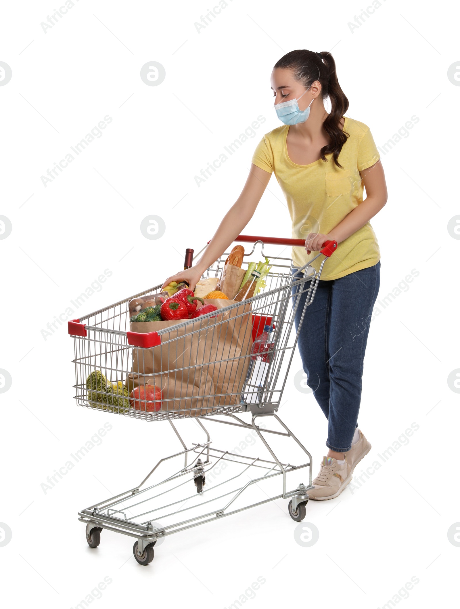 Photo of Woman with protective mask and shopping cart full of groceries on white background