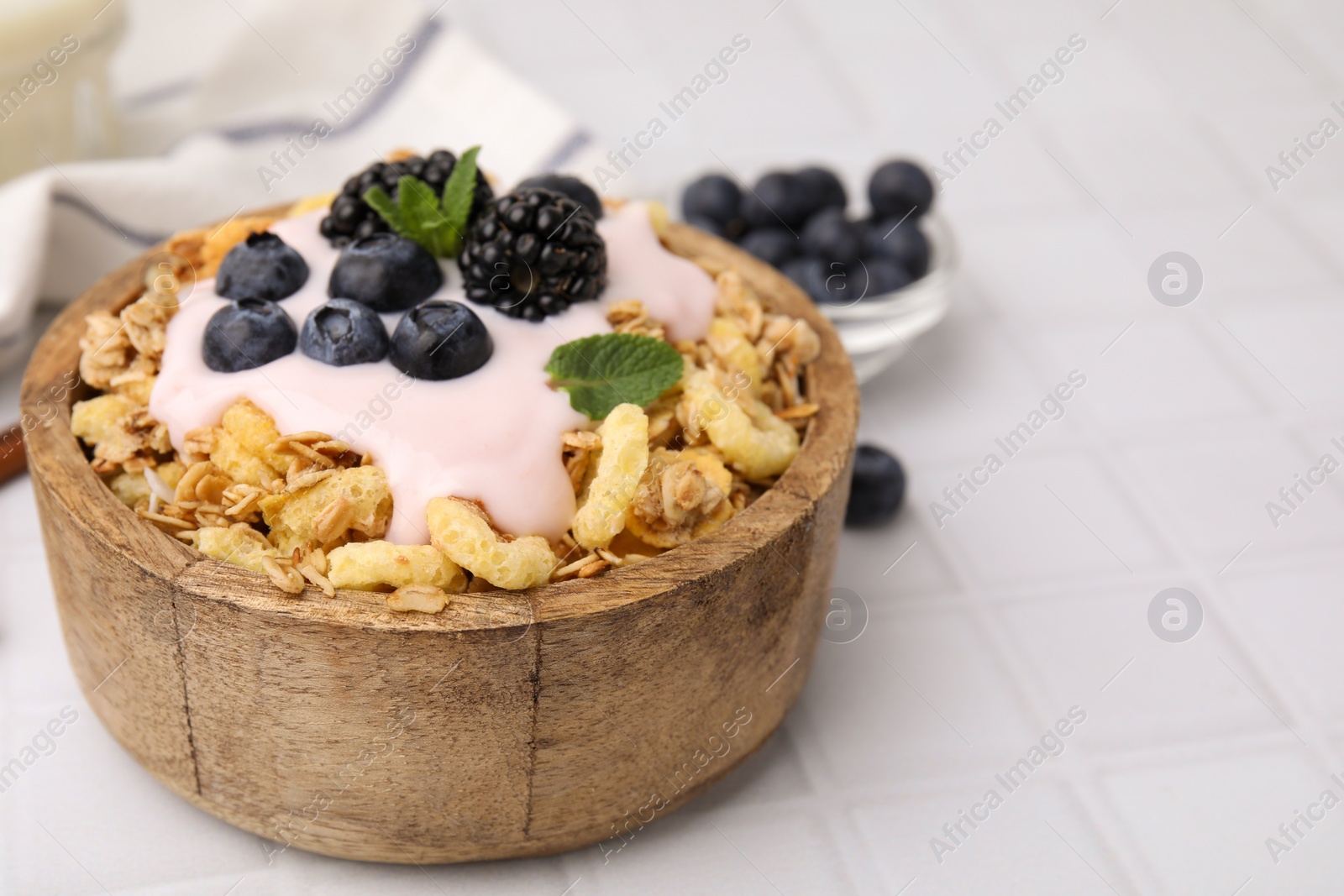 Photo of Tasty granola, yogurt and fresh berries in bowl on white tiled table, closeup with space for text. Healthy breakfast