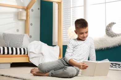 Photo of Little boy with book in stylish bedroom interior