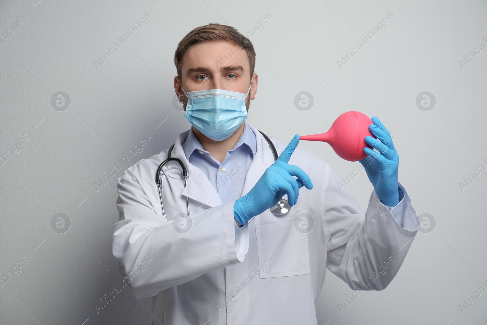 Photo of Doctor holding rubber enema on grey background