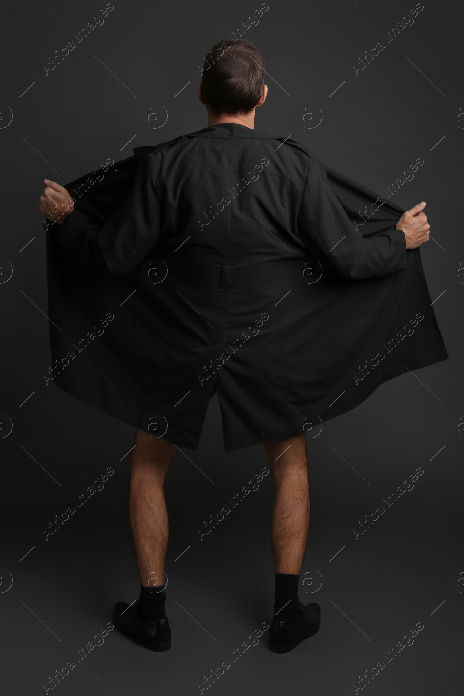 Photo of Exhibitionist exposing naked body under coat on black background, back view