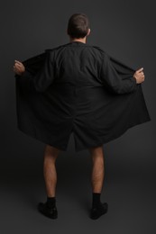Photo of Exhibitionist exposing naked body under coat on black background, back view