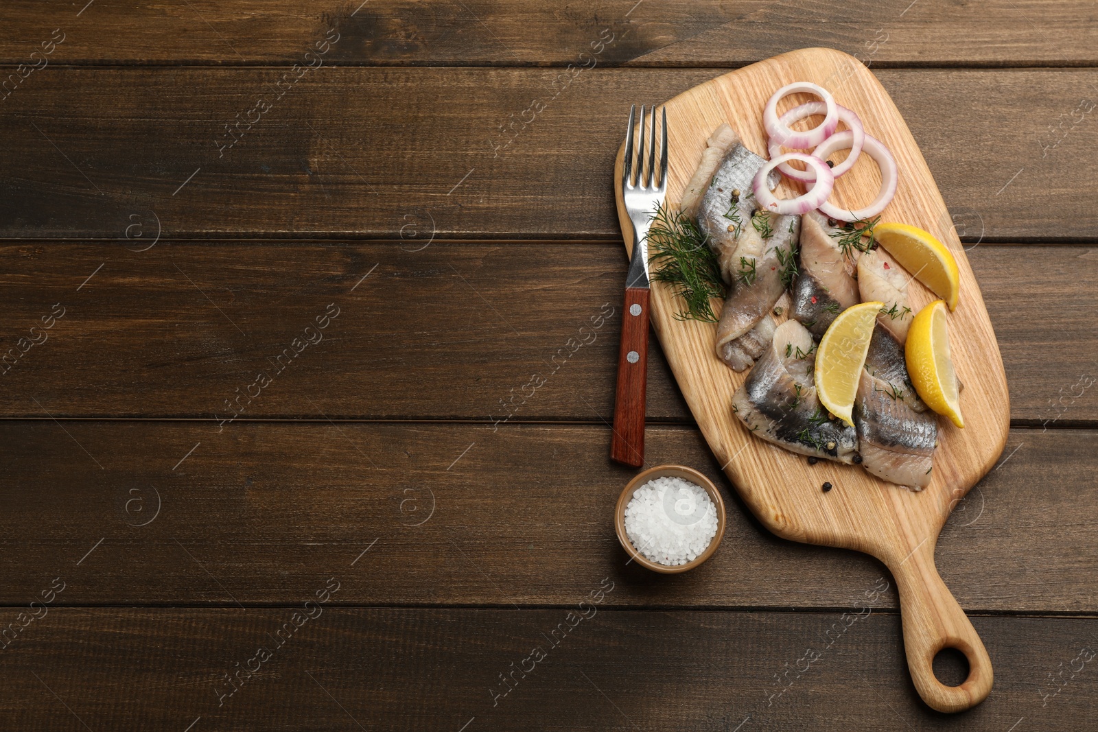 Photo of Sliced salted herring fillet served with dill, onion rings and lemon on wooden table, flat lay. Space for text