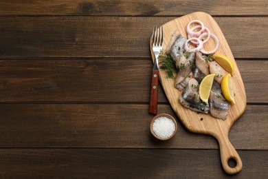 Photo of Sliced salted herring fillet served with dill, onion rings and lemon on wooden table, flat lay. Space for text