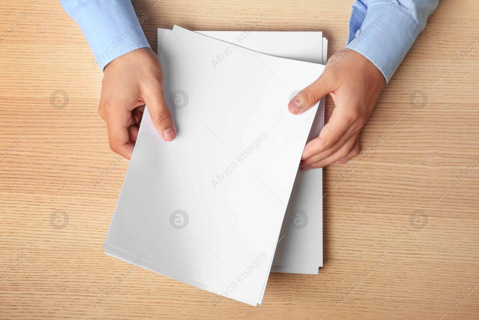 Photo of Man holding blank paper sheets for brochure at wooden table, top view. Mock up