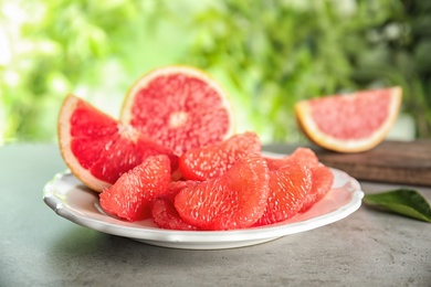 Photo of Plate with ripe grapefruit on table against blurred background