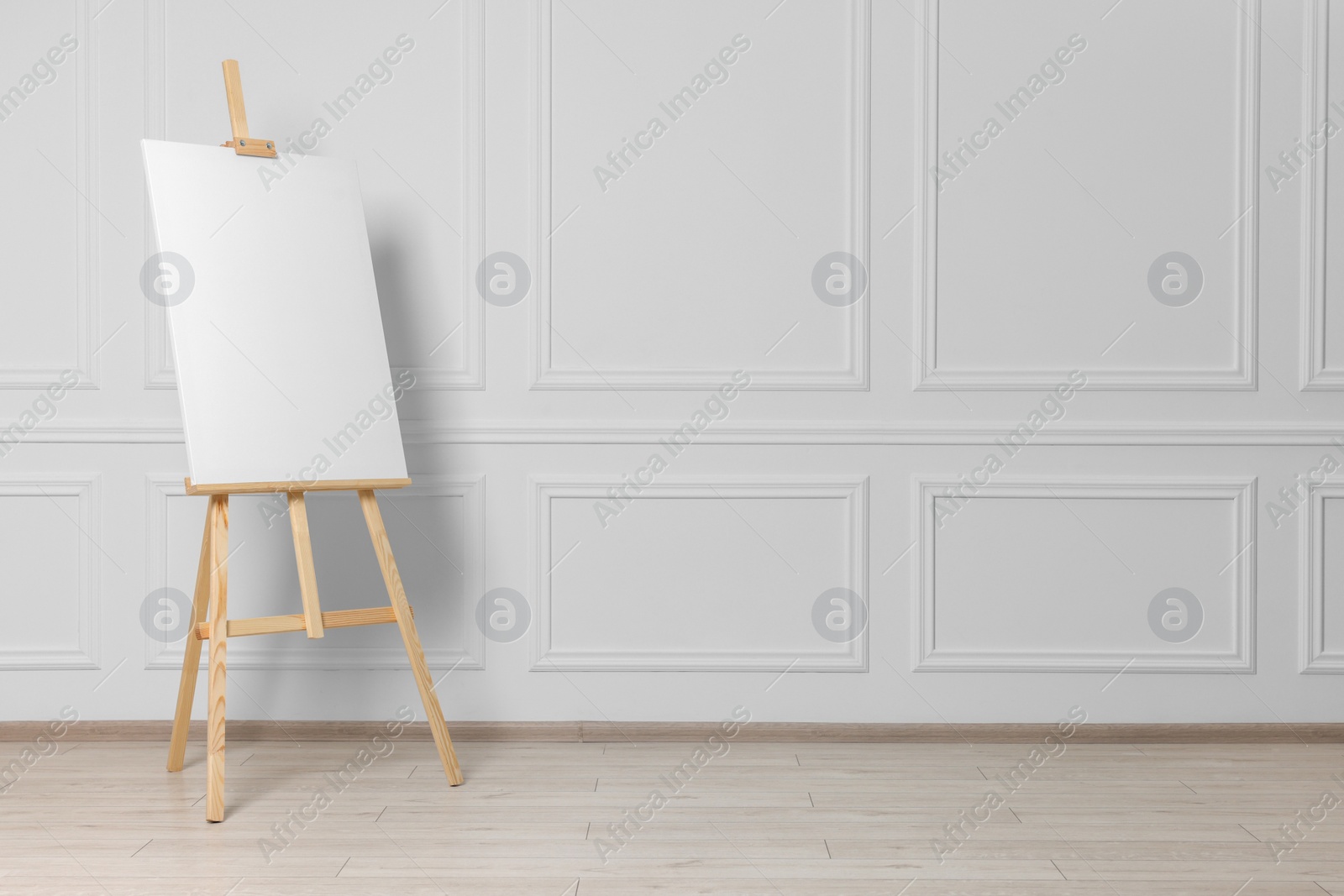 Photo of Wooden easel with blank canvas near white wall indoors. Space for text