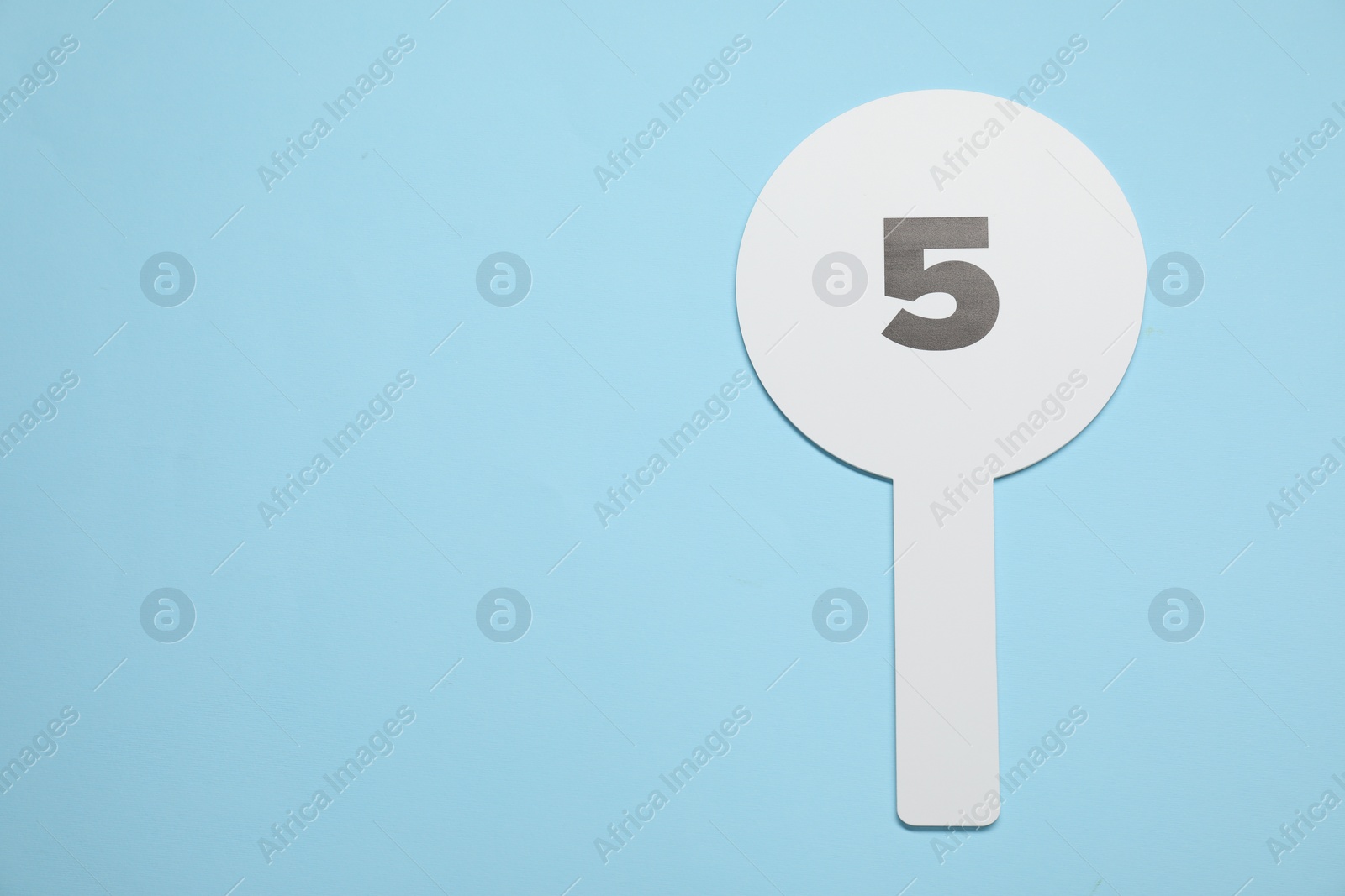 Photo of Auction paddle with number 5 on light blue background, top view. Space for text