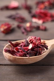 Spoon of dry hibiscus tea on wooden table, closeup