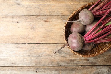 Photo of Raw ripe beets in wicker bowl on wooden table, top view. Space for text