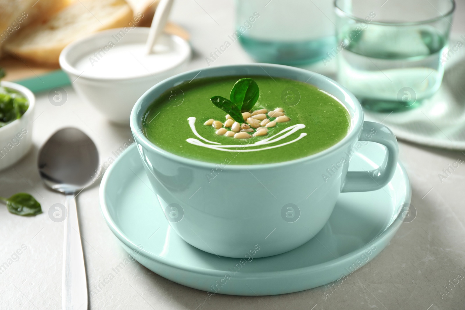 Photo of Cup of healthy green soup with fresh spinach on light table