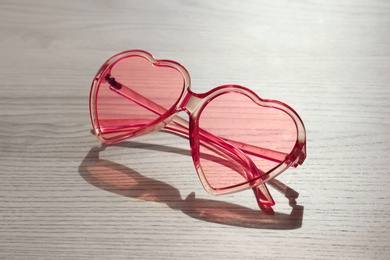 Stylish heart shaped sunglasses on wooden background