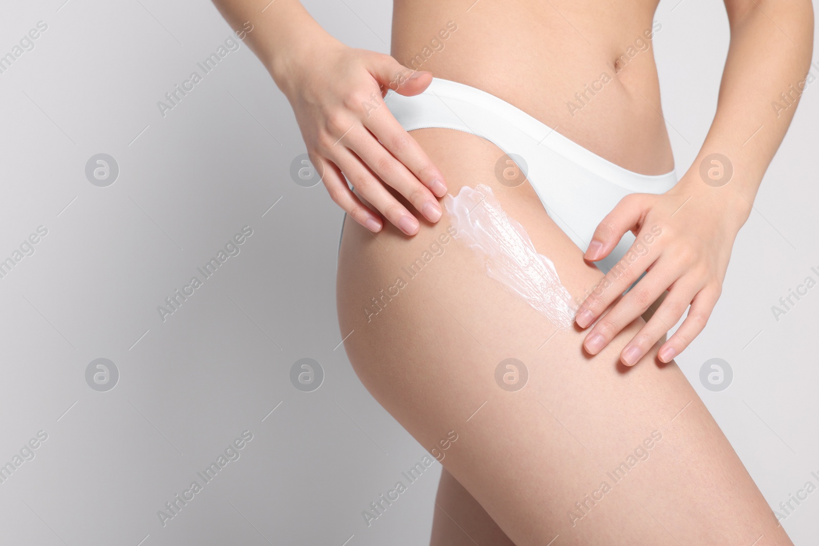 Photo of Woman applying body cream onto hip on light grey background, closeup. Space for text