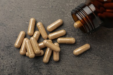 Photo of Overturned bottle with dietary supplement capsules on grey table, flat lay