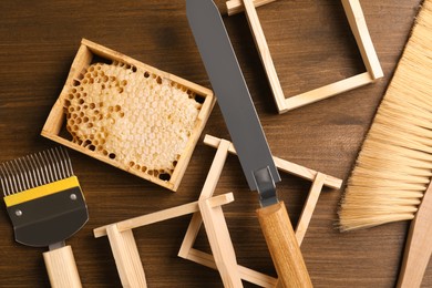 Photo of Honeycomb frames and beekeeping tools on wooden table, flat lay