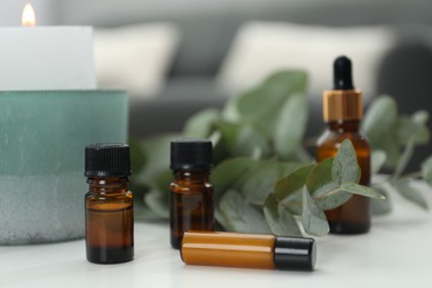 Aromatherapy. Bottles of essential oil, burning candle and eucalyptus leaves on white table