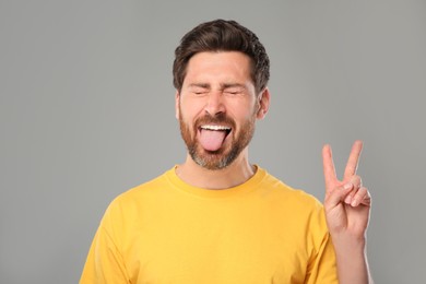 Photo of Man showing his tongue and V-sign on gray background