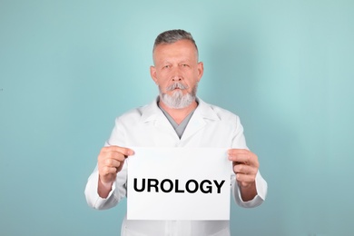 Male doctor holding paper with word UROLOGY on color background