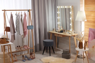 Makeup room. Stylish dressing table with mirror, chair and clothes rack indoors