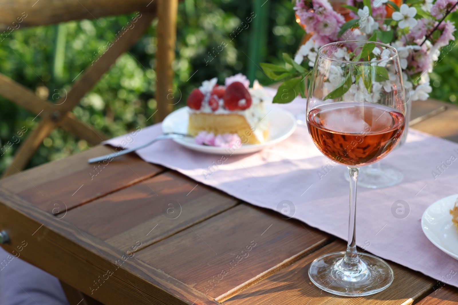 Photo of Glass of rose wine on table served for romantic date in garden