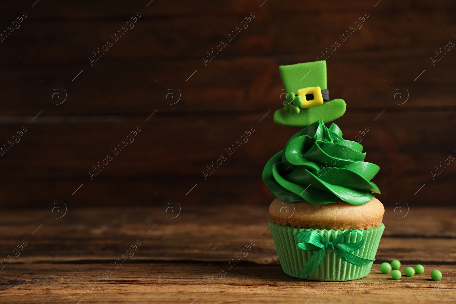 Photo of Delicious decorated cupcake on wooden table, space for text. St. Patrick's Day celebration