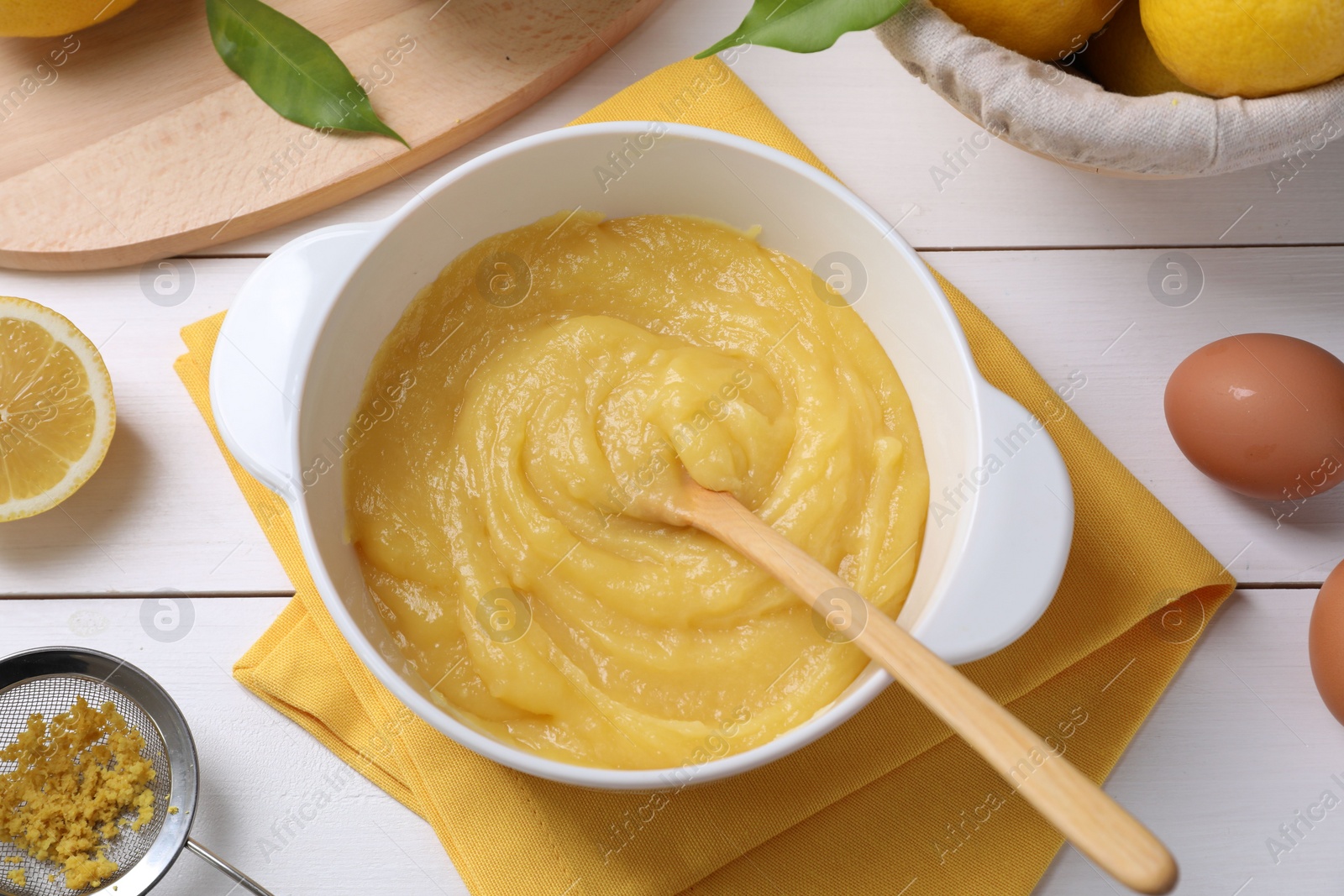 Photo of Delicious lemon curd in bowl, ingredients, spoon and sieve on white wooden table, flat lay