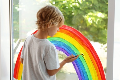 Photo of Little boy drawing rainbow on window. Stay at home concept