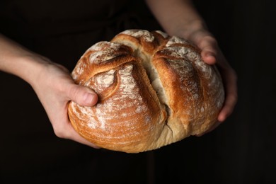 Photo of Woman holding loaf of tasty wheat sodawater bread on dark background, closeup