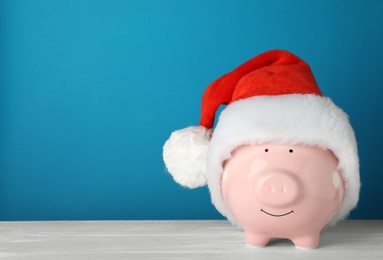 Photo of Piggy bank with Santa hat on table. Space for text