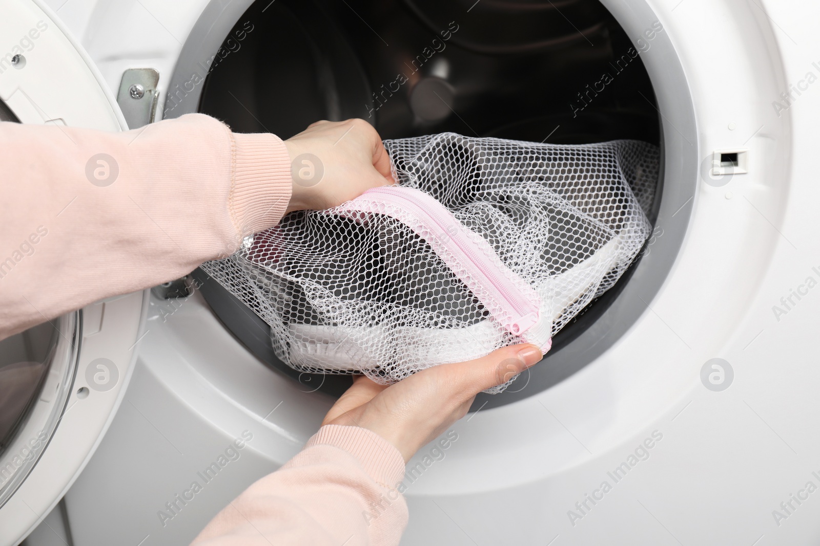 Photo of Woman putting stylish sneakers into washing machine, closeup