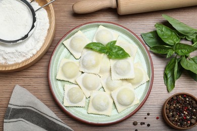 Photo of Uncooked ravioli, basil and peppercorns on wooden table, flat lay