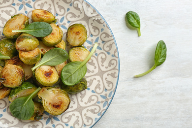Photo of Delicious roasted brussels sprouts with basil on white wooden table, flat lay