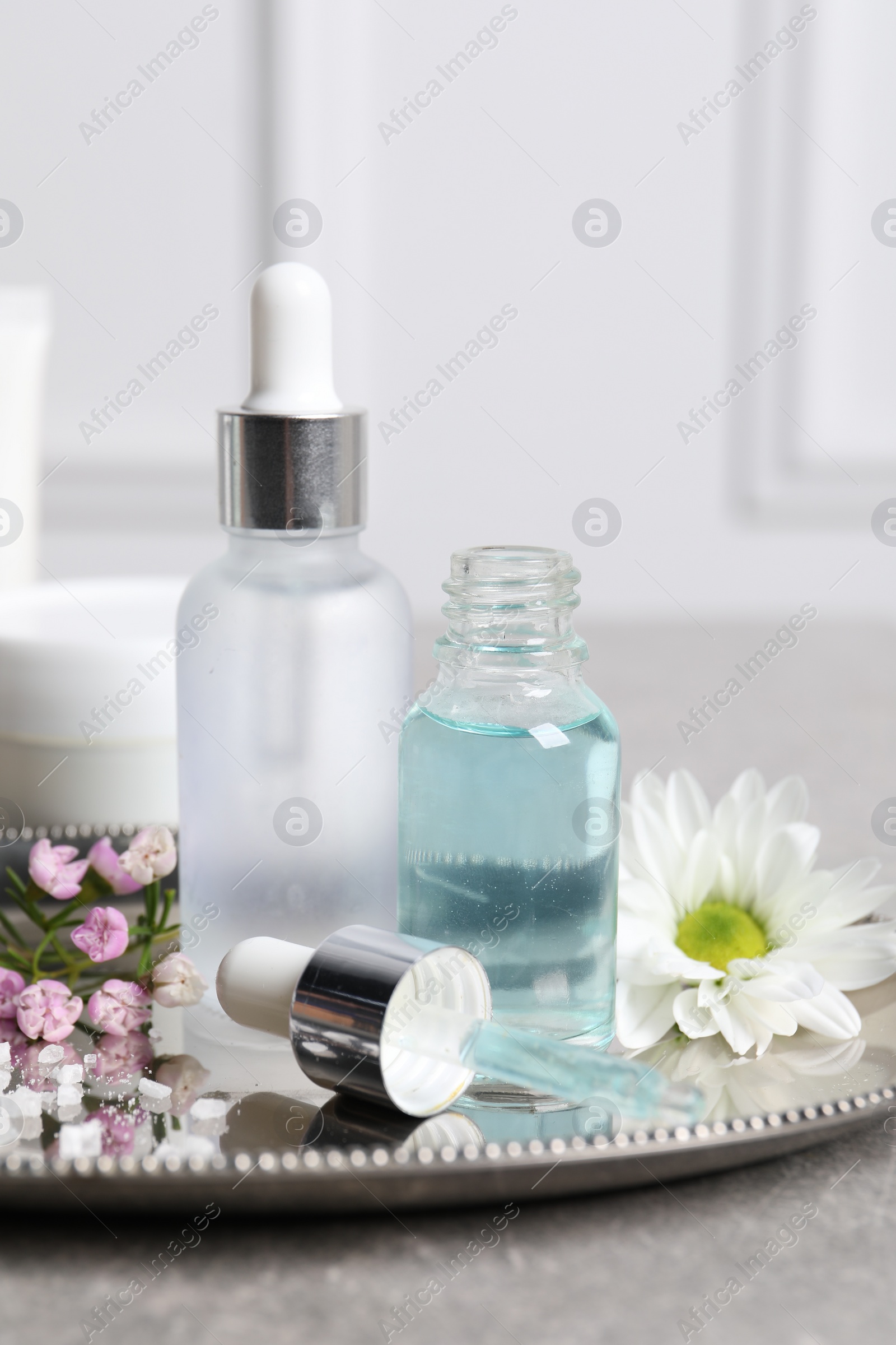 Photo of Bottles of cosmetic serum and beautiful flowers on gray table