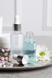 Bottles of cosmetic serum and beautiful flowers on gray table